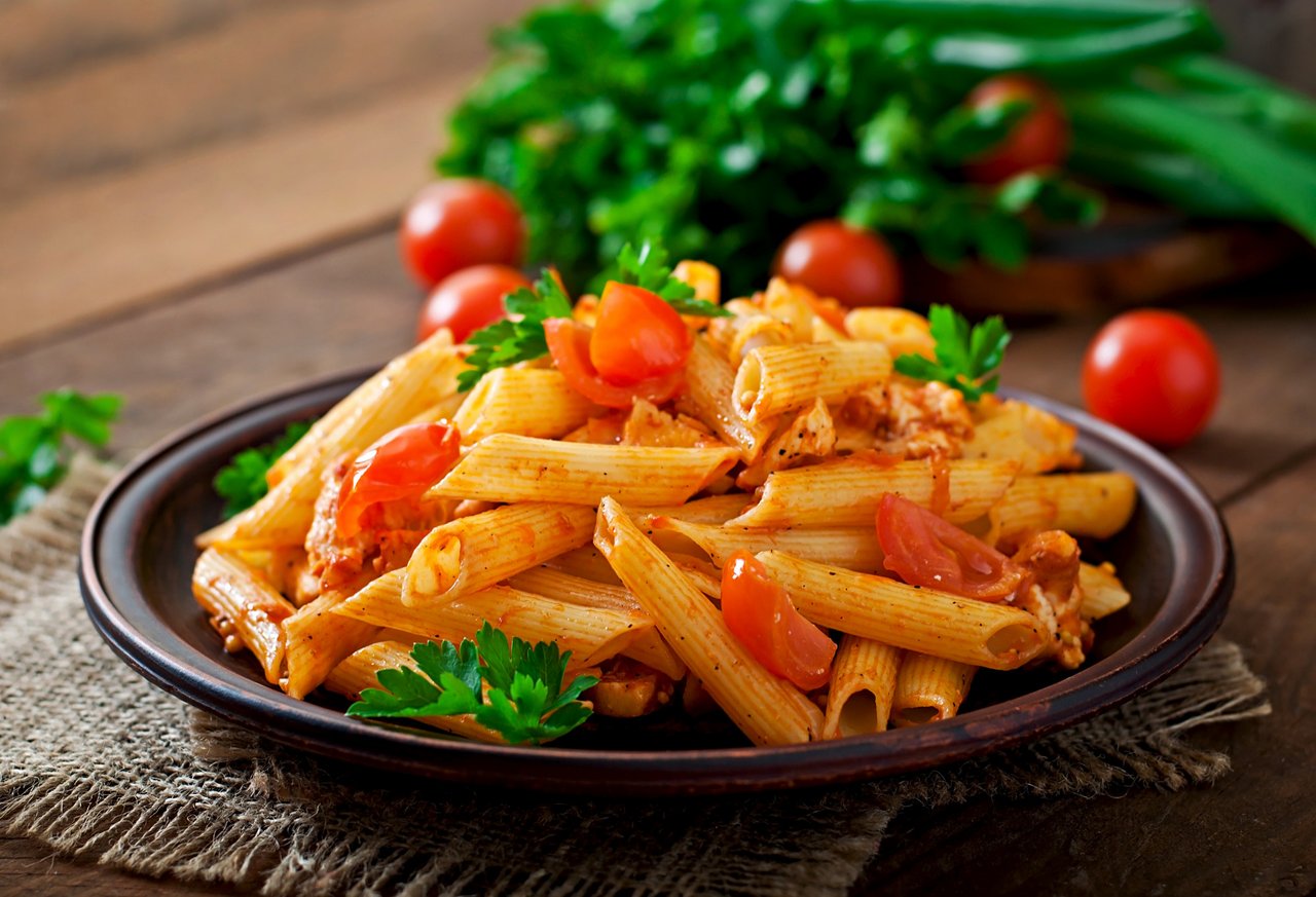 pasta-di-penne-in-salsa-di-pomodoro-con-pollo-e-pomodori-su-un-tavolo-di-legno.jpg