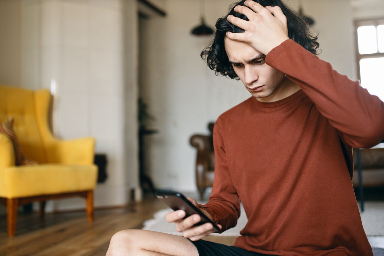 frustrated-young-man-having-stressed-facial-expression-keeping-hand-his-head-holding-cell-phone-reading-bad-news.jpg