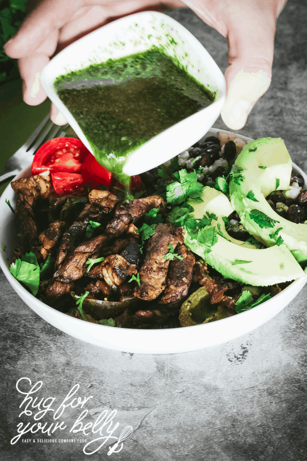 pouring chimichurri sauce over fajita steak bowl