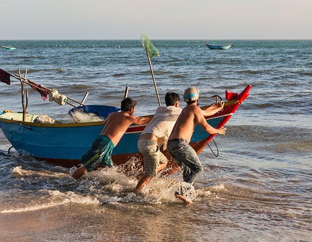 Putting the fishing boat into the water at the Beach in Hàm Tiến