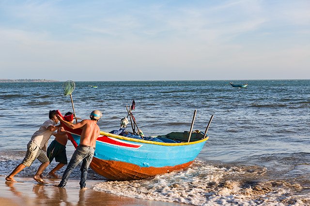 Putting the fishing boat into the water at the Beach in Hàm Tiến