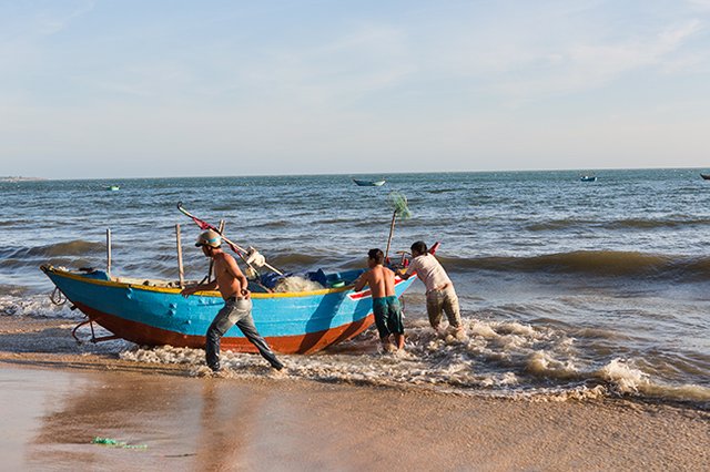 Putting the fishing boat into the water at the Beach in Hàm Tiến