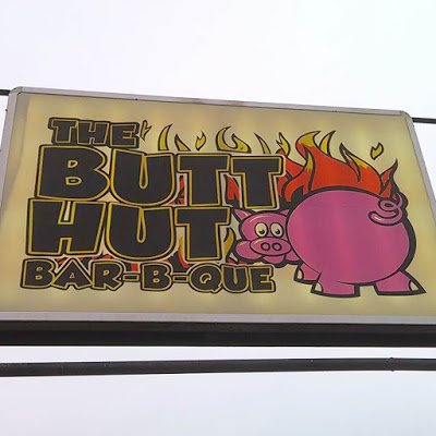 Sign reads "The Butt Hut Bar-b-que" and has a pig seen from butt.