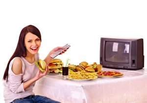 Mujer comiendo comida rápida y viendo la televisión.