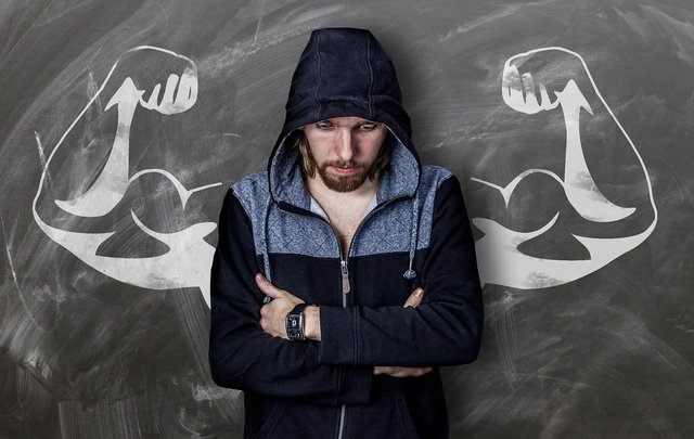 apparently weak man with muscular arms painted on wall behind him