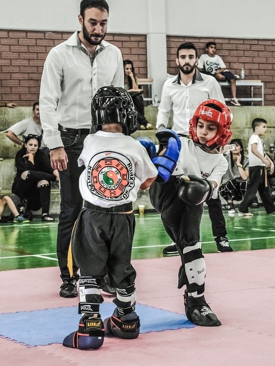 2 kids competing in kick-boxing with a referee watching