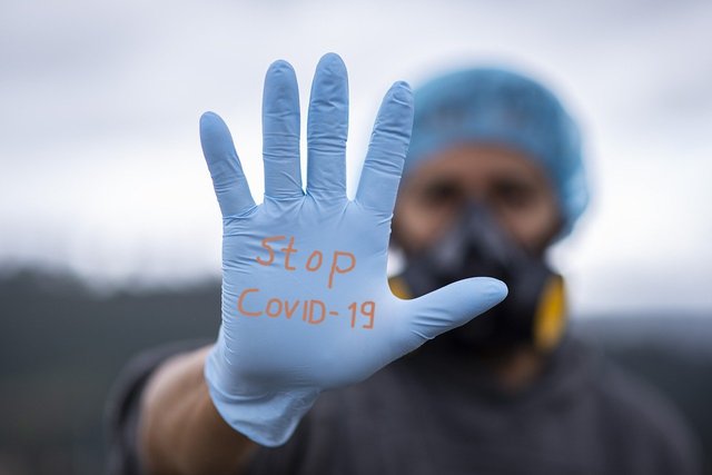 person in haircover and mask with gloved hand forward with "Stop CoViD-19"
