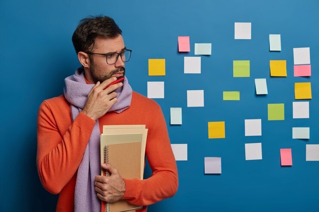 pensive-brunet-male-student-holds-chin-has-thick-bristle-holds-necessary-notepads-wears-scarf-sweater_273609-34102.jpg