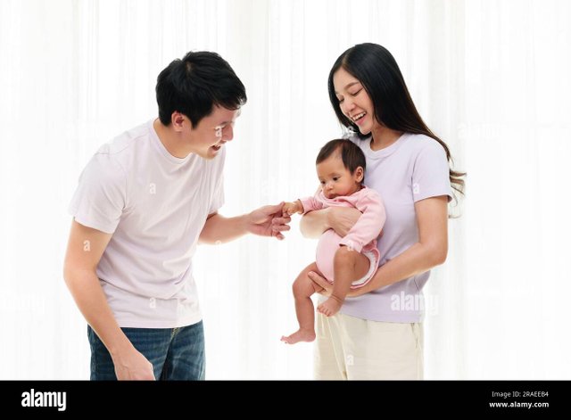 cheerful-father-and-mother-holding-and-playing-with-newborn-baby-on-white-window-background-happy-family-concept-2RAEEB4.jpg