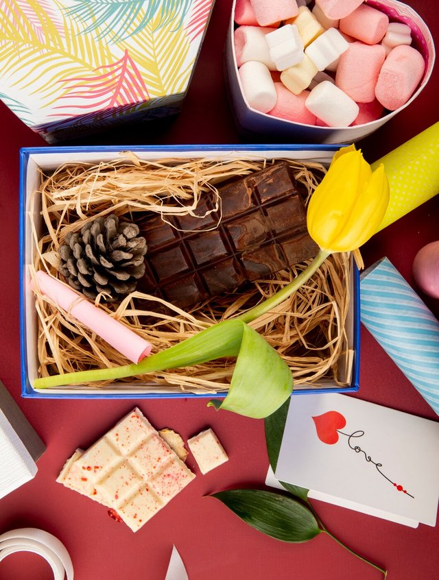 top-view-open-present-box-with-yellow-color-tulip-flower-dark-chocolate-bar-cone-straw-heart-shaped-box-filled-with-marshmallow-dark-red-table_141793-8787.jpg