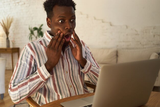 funny-shocked-young-dark-skinned-man-casual-clothes-having-desperate-look-holding-hands-cheeks-sitting-table-with-laptop_343059-2524.jpg