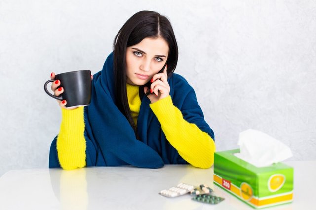 sick-young-woman-covered-with-blanket-holding-cup-tea-sitting-table_231208-1139.jpg