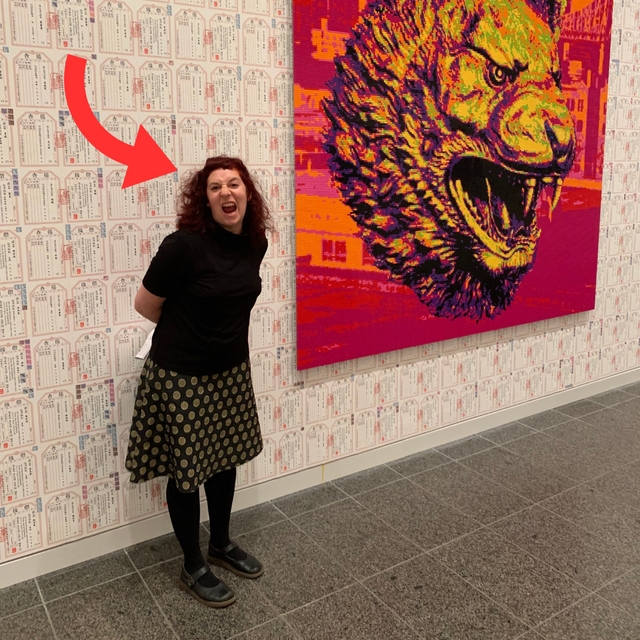 woman mimiking the face of a tiger in front of an artwork of Ai Weiwei