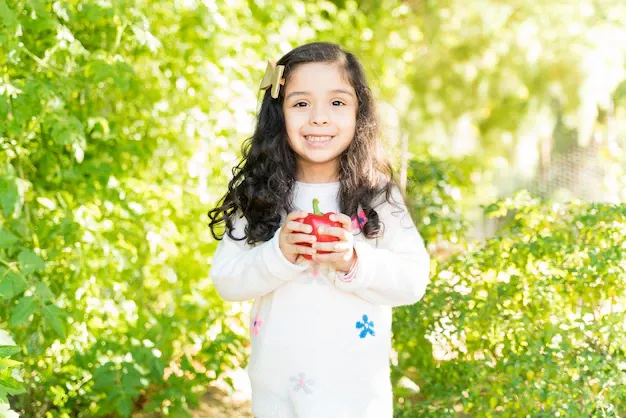 cute-smiling-hispanic-girl-holding-fresh-bell-pepper-while-standing-farm_662251-597.webp