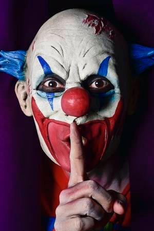 85893259-a-scary-evil-clown-peering-out-from-a-purple-stage-curtain-with-his-forefinger-in-front-of-his-lips-.jpg