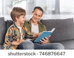 stock-photo-happy-father-and-son-reading-book-together-while-sitting-on-couch-746876647.jpg