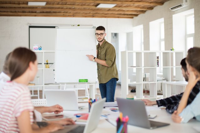 young-businessman-eyeglasses-shirt-standing-near-board-while-thoughtfully-discussing-new-project-with-colleagues-group-people-working-together-modern-office.jpg