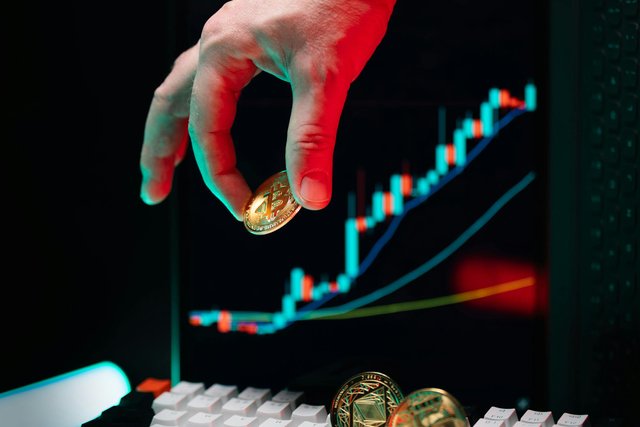 free-photo-of-hand-holding-bitcoin-over-rising-chart-on-screen.jpeg