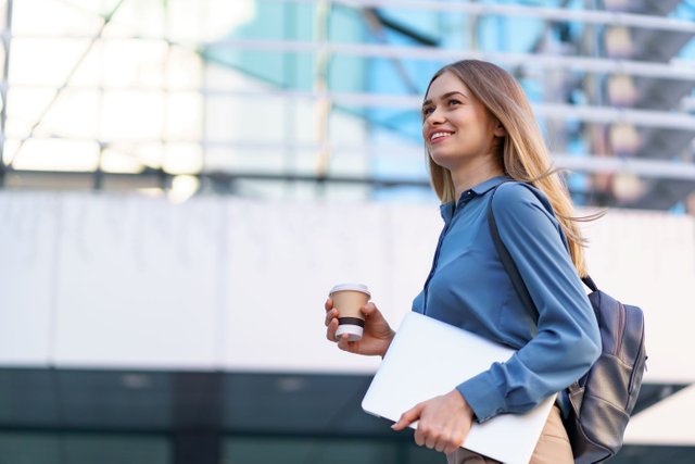 blonde-young-woman-smiling-portrait-holding-laptop-coffee-wearing-blue-gentle-shirt-modern-building1.jpg