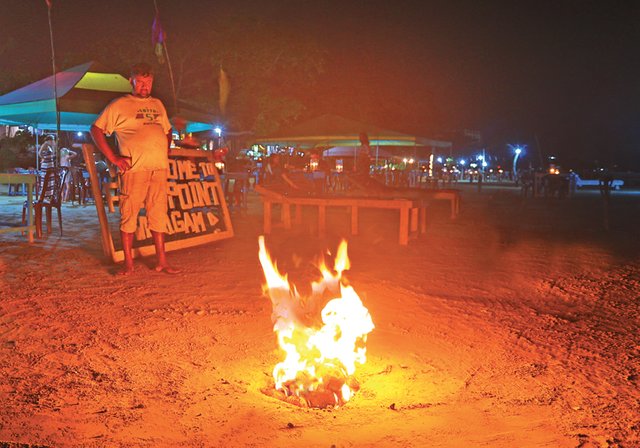 The unique setup for the BBQ. Manjula Chrishantha watches as the coconut shells are burnt for charcoal.jpg