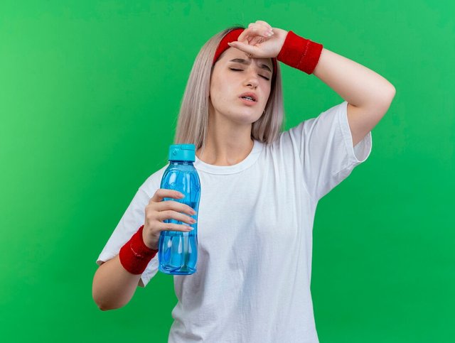 aching-young-sporty-woman-with-braces-wearing-headband-wristbands-puts-hand-forehead-holds-water-bottle-isolated-green-wall_141793-95565.jpg