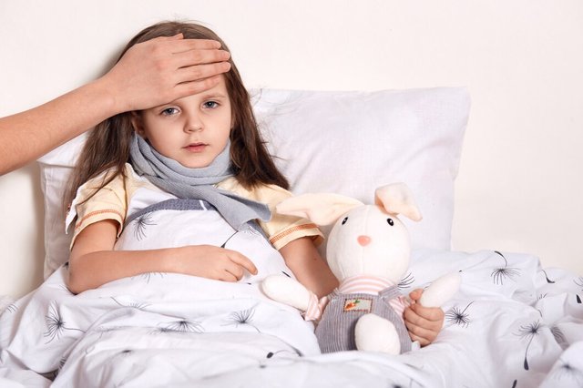 indoor-shot-little-girl-with-fair-hair-lying-her-bed-hugging-favourite-toy-having-unknown-hand-forehead-checking-temperature_176532-9504.jpg