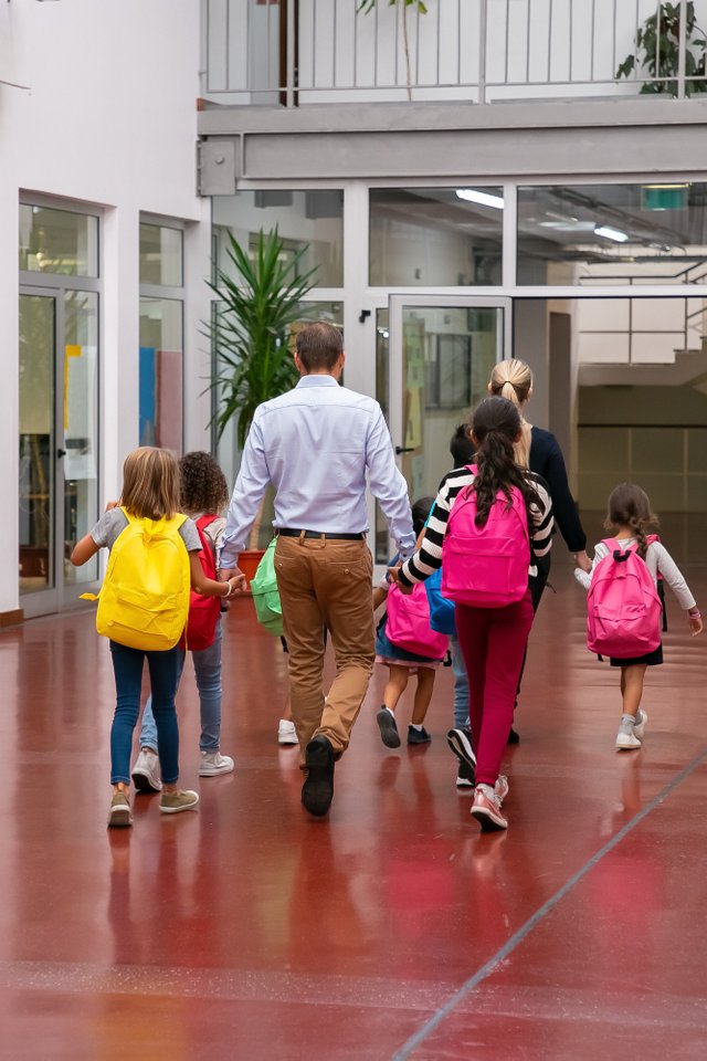 schoolkids-with-bright-backpacks-walking-through-school-hallway-holding-hands-teachers.jpg