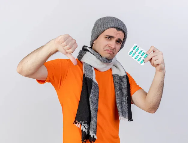 sad-young-ill-man-wearing-winter-hat-with-scarf-holding-pills-showing-thumb-down-isolated-white_141793-56497.webp