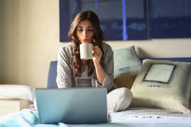 woman-in-grey-jacket-sits-on-bed-uses-grey-laptop-935743.jpg