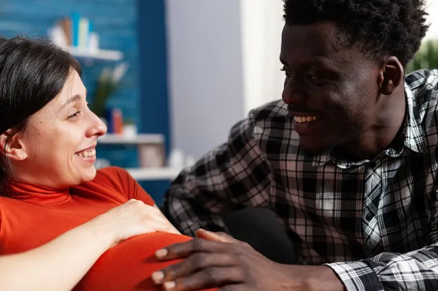 closeup-smiling-interracial-young-couple-expecting-newbornwhile-sitting-home-love-relaxed-married-partners-waiting-unborn-child-while-african-american-husband-feeling-caucasian-pregnant_482257-37890.webp