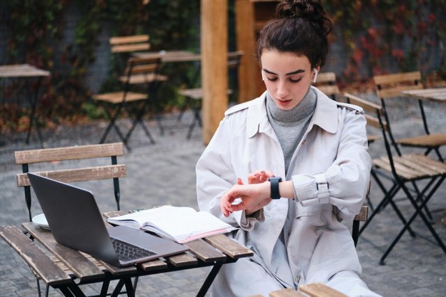 attraente-ragazza-bruna-in-trench-usando-con-sicurezza-smartwatch-che-studia-nella-caffetteria-sulla-strada-della-citta.jpg