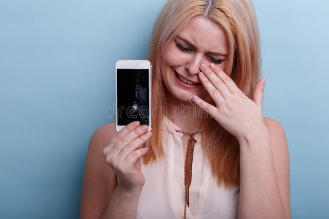 chica-joven-llorando-sosteniendo-un-teléfono-móvil-quebrado-disponible-primer-en-fondo-azul-107303091.jpg