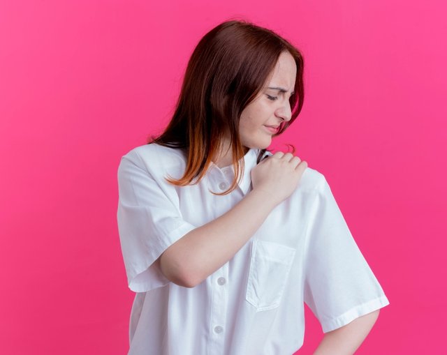 injured-young-redhead-girl-grabbed-shoulder-isolated-pink-wall_1.jpg