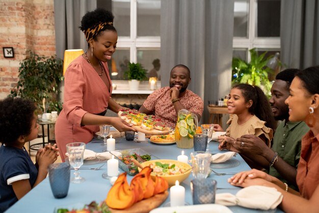 young-african-woman-putting-wooden-board-with-appetizing-homemade-sandwiches-festive-table-burning-candles-other-food_274679-25486.jpg