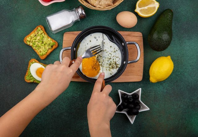 top-view-fried-egg-frying-pan-wood-kitche-board-with-toasted-bread-slices-with-avocado-pulp-black-olives-green_141793-17401.jpg