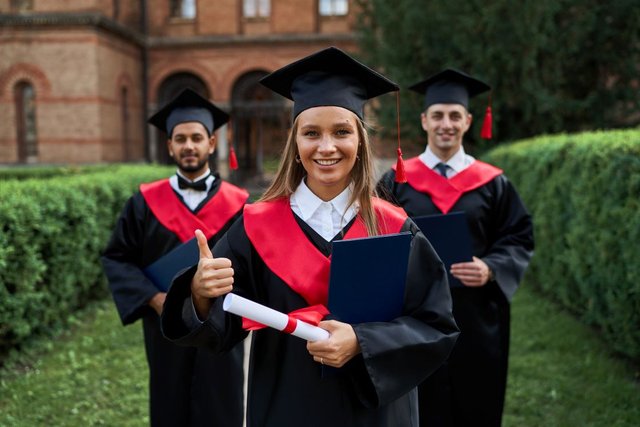 graduate-female-shows-like-with-her-friends-graduation-gowns-holding-diploma-smiling-camera1.jpg