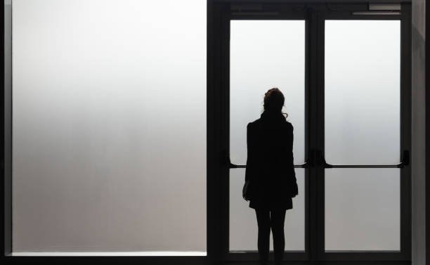 depressed-woman-waiting-in-front-a-glass-door-in-a-white-room-ready-picture-id912134542.jpg
