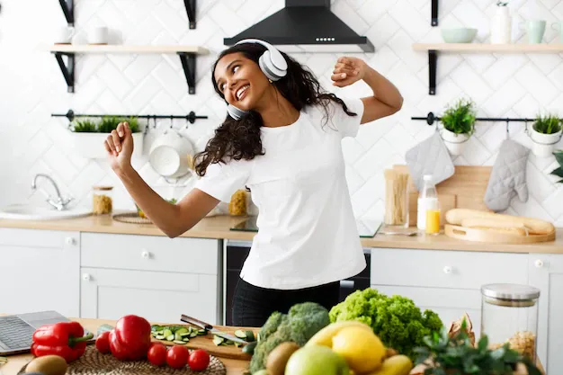 smiled-mulatto-woman-big-wireless-headphones-is-dancing-near-table-full-vegetables-fruits_8353-10296.webp