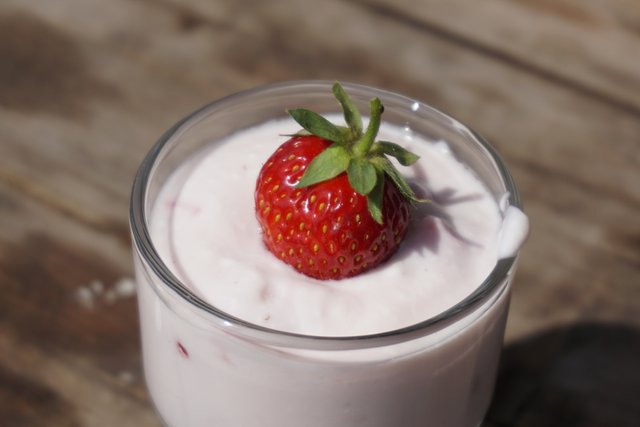 Close-up of a small glass filled with yoghurt, which contains fresh chopped strawberries. On the yoghurt is a very good-looking strawberry on the whole decorated with a stalk approach decorative.