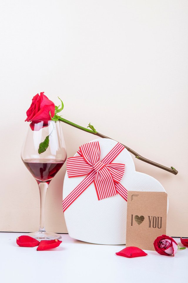 side-view-glass-wine-red-color-rose-heart-shaped-gift-box-tied-with-bow-with-small-postcard-white-background_141793-8018.jpg