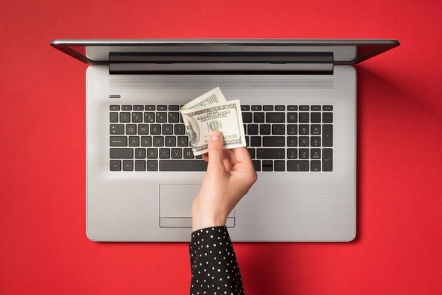 photo-grey-laptop-hand-holding-hundred-dollars-isolated-red-backdrop_352249-6660.jpg