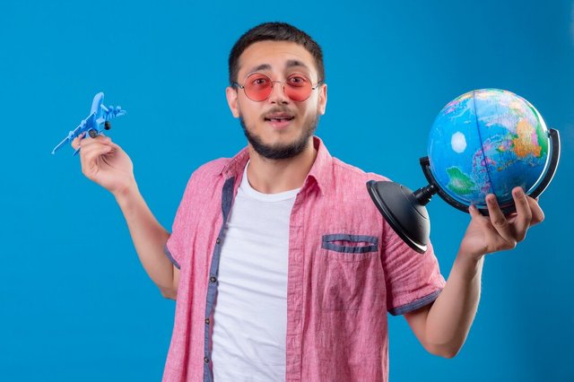 young-handsome-traveler-guy-holding-wearing-sunglasses-holding-toy-airplane-globe-looking-positive-happy-smiling-friendly-standing-blue-background_141793-14835.jpg