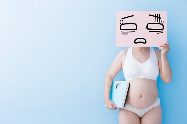 chubby-woman-holding-scale-and-sign-to-cover-face.jpg