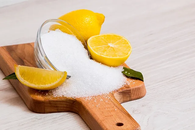 Citric_acid_powder_in_a_bowl_and_halved_lemons_on_a_chopping_board.webp