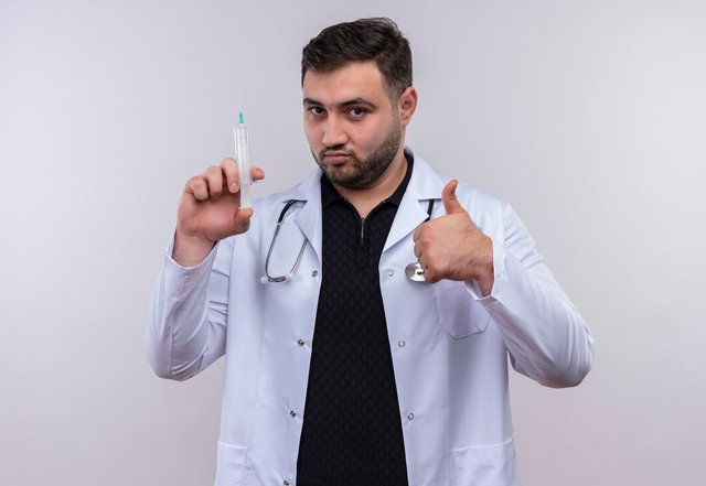 young-bearded-male-doctor-wearing-white-coat-with-stethoscope-holding-syringe-smiling-confident-showing-thumbs-up_141793-28182.jpg