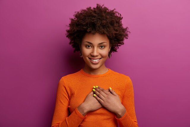 pleased-girl-orange-jumper-presses-palms-heart-makes-thankful-gesture-touched-with-cordial-congratulations-smiles-positively-isolated-purple-wall-acknowledgement-concept_273609-42652.jpg