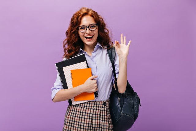 red-haired-lady-eyeglasses-holds-books-shows-ok-sign.jpg