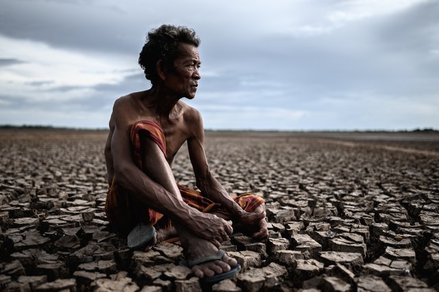 elderly-man-sat-hugging-his-knees-bent-dry-soil-looked-sky.jpg