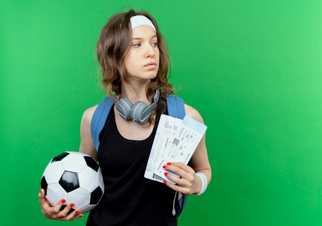 young-fitness-girl-black-sportswear-with-backpack-headband-holding-soccer-ball-air-tickets-looking-aside-puzzled-standing-green-wall_141793-55614.jpg