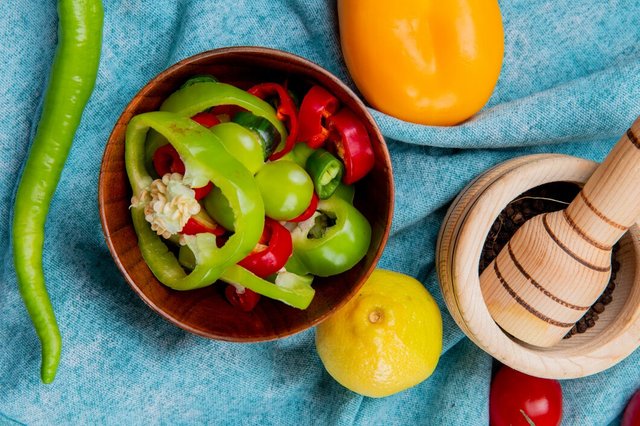 top-view-sliced-peppers-bowl-with-whole-ones-tomato-lemon-with-black-pepper-garlic-crusher-blue-cloth_141793-12805.jpg